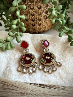 These exquisite earrings are handcrafted with intricate inlay work, featuring vibrant semi-precious stones set in a rich, red background. The intricate design is adorned with glistening crystals and accented with delicate crystal drops, creating a stunning and eye-catching pair of earrings. Crafted with meticulous attention to detail, these earrings are a true work of art. The inlay technique showcases the skill and artistry of the craftsperson, resulting in a unique and timeless piece of jewelry. Whether for a special occasion or as an everyday accessory, these earrings are sure to elevate any outfit and add a touch of elegance. Perfect for those who appreciate exquisite craftsmanship and one-of-a-kind designs. ------------------------------------------------------------------------------ Jeweled Drop Danglers For Gift, Multicolor Metal Jewelry With Intricate Design, Fusion Style Jeweled Dangle Jewelry, Fusion Style Jewelry With Matching Earrings For Festive Occasions, Silver Jeweled Earrings For Festive Occasions, Fusion Jeweled Dangle Jewelry, Festive Fusion Jewelry With Matching Earrings, Fusion Style Jeweled Dangle Earrings, Fusion Jeweled Dangle Earrings