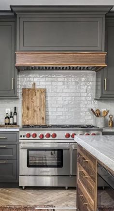 a kitchen with gray cabinets and white marble counter tops, an oven and stove hood