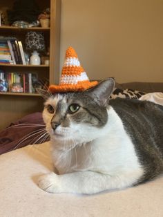 a cat laying on top of a bed wearing a small orange and white crocheted hat