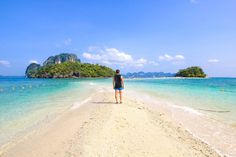 a person standing on the beach looking out at an island in the water and sand