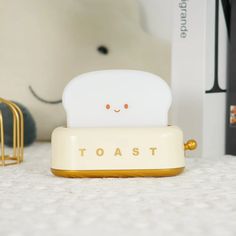 a white toaster sitting on top of a table next to a golden rack and book