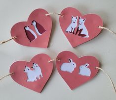 four heart shaped paper cutouts with animals on them hanging from twine strings in the shape of hearts