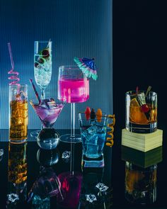 several different types of cocktails in glass vases on a table with blue and black background