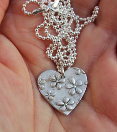 Heart flower necklace, floral heart pendant, mothers day pendant, garden necklace, embossed flower necklace, floral necklace, daisy necklace Floral heart pendant lovingly handcrafted in solid silver. The heart is decorated with a beautiful raised daisy flower pattern. It would make a stunning gift for mother's day or a gardener or just anyone who loves flowers. It is inspired by the beautiful flowers in my York wildlife garden. The pendant is hung on a sterling silver ball chain, finished with a sterling silver clasp. The pendant is approximately 2cm by 1.8cm. All my nature jewellery raises funds to support my hedgehog hospital caring for poorly and injured wild hedgehogs.  Your pendant will be gift boxed and tied with pretty ribbon. I also enclose a rescue hedgehog postcard and informatio Charming Flower Pendant Necklace, Flower Charm Necklace As Gift For Mom, Flower Charm Pendant Necklace Gift For Mom, Mother's Day Flower Shaped Jewelry With Heart Charm, Mother's Day Flower Jewelry With Heart Charm, Mother's Day Jewelry With Heart Charm And Flower Shape, Mother's Day Flower Pendant Charm Necklace, Flower Pendant Necklace For Mother's Day, Anniversary Necklace With Heart Pendant And Flower Charm