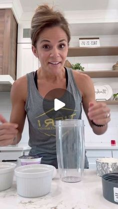 a woman standing in front of a blender filled with ingredients for a smoothie