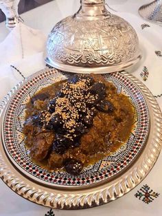 a silver plate topped with meat covered in gravy next to a serving dish