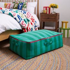 a green suitcase sitting on top of a rug next to a bed with pillows and blankets