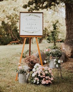 a sign that is in the grass near some flowers and potted plants on it