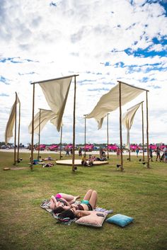 two women are laying on the grass under some umbrellas