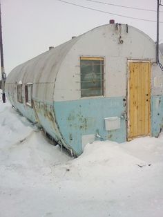 an old train car sitting in the snow next to a building with a door on it