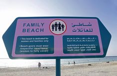 a family beach sign on the beach with people in the water and sand behind it