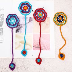 four crocheted flowers are shown on top of an open book, next to each other