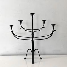 a black metal candelabra with five candles in it's center on a white surface