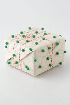 a present wrapped in white paper with green pom - poms on the top