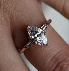 a woman's hand holding a ring with a large diamond in the center and two baguettes on each side