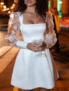 a woman in a short white dress holding a drink and posing for the camera with her hands on her hips