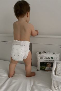 a baby in diapers standing on top of a bed next to a pack of diapers