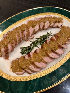 sliced meat with sauce and herbs on a green and gold plated serving platter