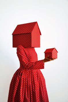 a woman in a red polka dot dress and hat holding a small house shaped box