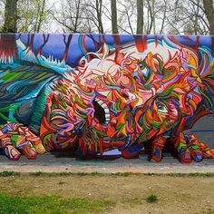 a large colorful animal painted on the side of a wall next to grass and trees