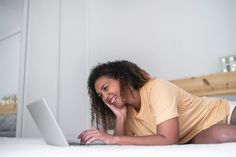 a woman laying on the bed with her laptop computer in front of her, smiling