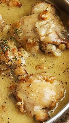 a pan filled with chicken and gravy on top of a table next to silverware