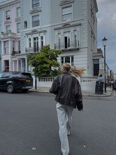 a woman walking down the street with her hair blowing in the wind and cars parked on the side of the road