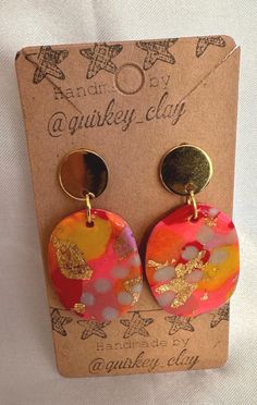 a pair of pink and yellow earrings on top of a brown card with gold accents