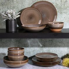 there are many plates and bowls on the shelf next to each other, including one that has a plant in it