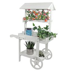 a small white cart with flowers and plants on the top, sitting next to a potted plant