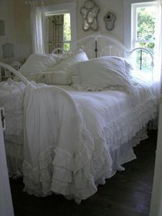 a white bed with ruffled bedspread and pillows