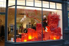 a store window with many red presents in the front and behind it is a mannequin