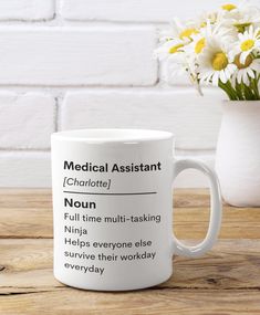 a white coffee mug sitting on top of a wooden table next to a vase with flowers