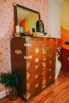 an old dresser has been decorated with gold leafy designs and is next to a potted plant