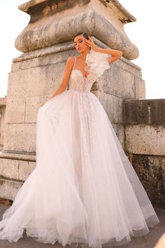 a woman in a wedding dress standing next to a stone structure with her hands on her head