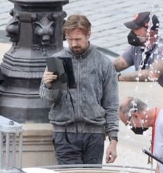 a man standing next to a fountain with water shooting out of his face and holding a book