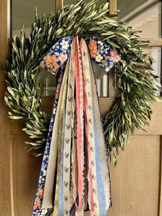 a wreath with ribbons hanging from it's side on the front door, next to a mirror