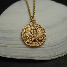 Hand carved dainty pendant from a medieval coin.Byzantine coin reproduction of Phocas (602-610 A.D.), emperor of the Byzantine Roman empire. Originally minted in Constantinople (Istanbul).Latin inscription: "ON FOCAS PЄRP AVI"• Hand carved charm.• Solid yellow bronze also called jeweler gold bronze charm.• Coin is 1/2"• Signed in the back by artist.• Soldered eyelet on top.• 14k gold filled chain.• Gold filled has 100 times more gold than plated. Does not rub off.• Lobster claw clasp.• Nickel fr Antique Gold Coin Necklace Handmade, Handmade Byzantine Style Necklace, Byzantine Style Medallion Coin Necklace, Medieval Historical Design Gold Jewelry, Handmade Byzantine Round Necklace, Medieval Style Gold Engraved Necklace, Ancient Gold Coin Necklace, Byzantine Necklace With Coin Pendant As Gift, Byzantine Coin Necklace As A Gift