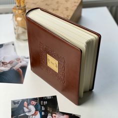 an open book sitting on top of a white table next to photos and a vase