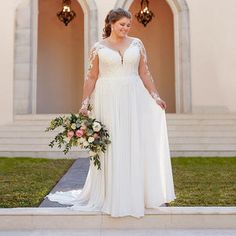 a woman standing in front of a building wearing a white dress and holding a bouquet