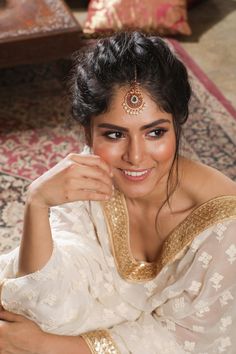 a woman wearing a white sari sitting on top of a rug