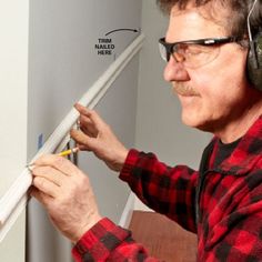 a man wearing headphones and ear muffs working on a piece of wood in his home