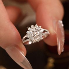 a woman's hand holding a diamond ring on top of her finger, with the tip of an acrylic nail sticking out