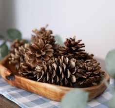 some pine cones in a wooden bowl on a checkered tablecloth with eucalyptus leaves