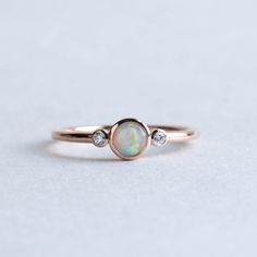 a white opal and diamond ring sitting on top of a gray surface with one stone in the middle