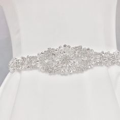 Otylia is elegantly tied with a ribbon, is crafted to radiate brilliance. Embellished with a sparkling crystal medallion, it perfectly complements a simple dress, adding a touch of dazzle to its simplicity. Embellishment measures approximately 12 inches long and 2.4 inches wide Designed with sparkling rhinestones Self-tie with a 106" ribbon Made-to-order, ships within 1 week from NY Elegant Evening Belts With Rhinestones, Elegant Rhinestone Belts For Formal Occasions, Elegant Embellished Bridal Belt For Party, Elegant Crystal Bridal Belt For Formal Occasions, White Crystal Sashes For Formal Occasions, Silver Rhinestone Sash For Formal Occasions, Silver Party Belts With Sashes, White Crystal Sash For Formal Occasions, Elegant White Sashes With Rhinestones