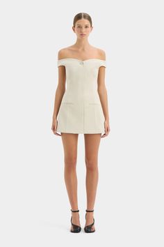 The Sandrine Off Shoulder Mini Dress in Ecru is an event-ready silhouette crafted from a premium Italian suiting fabric. Offering a structured silhouette, it features a subtle sweetheart neckline with a single button detail, off-shoulder straps, punctuated waist, and front pocket details. Pair back with heels for your next occasion.