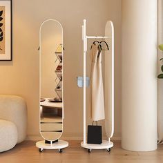 a white coat rack sitting next to a mirror on top of a wooden floor in a living room