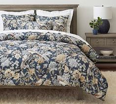 a bed with a blue and white comforter on top of it next to a night stand