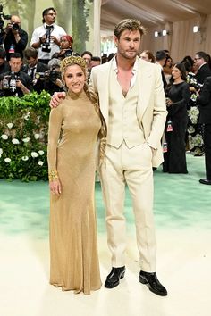 a man and woman standing next to each other on a white carpet with cameras in the background